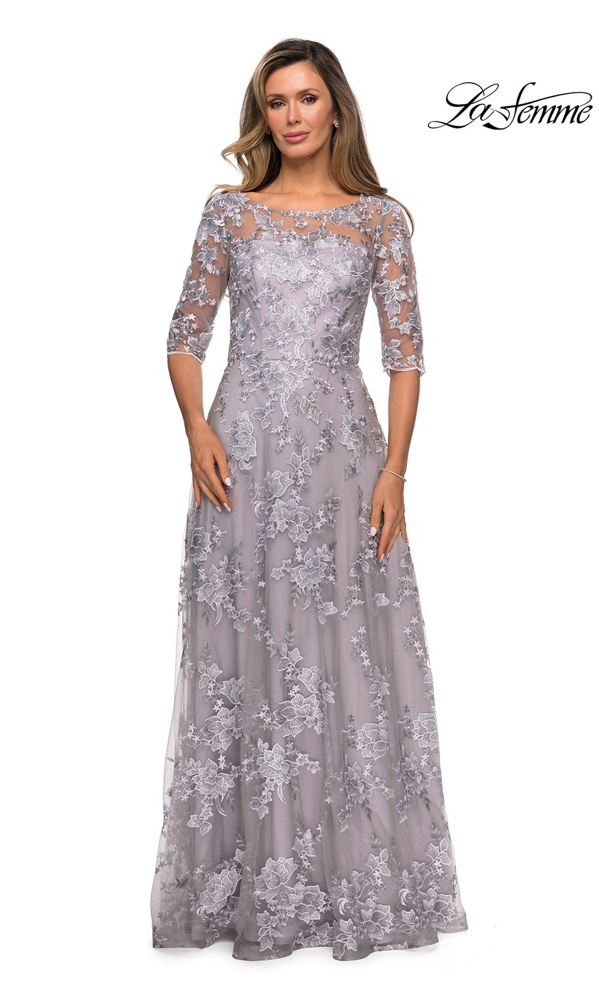 Woman poses in a Long Formal Dress: La Femme 27854—a floor-length, light lavender lace dress with three-quarter sleeves, floral embroidery, and sheer overlay.